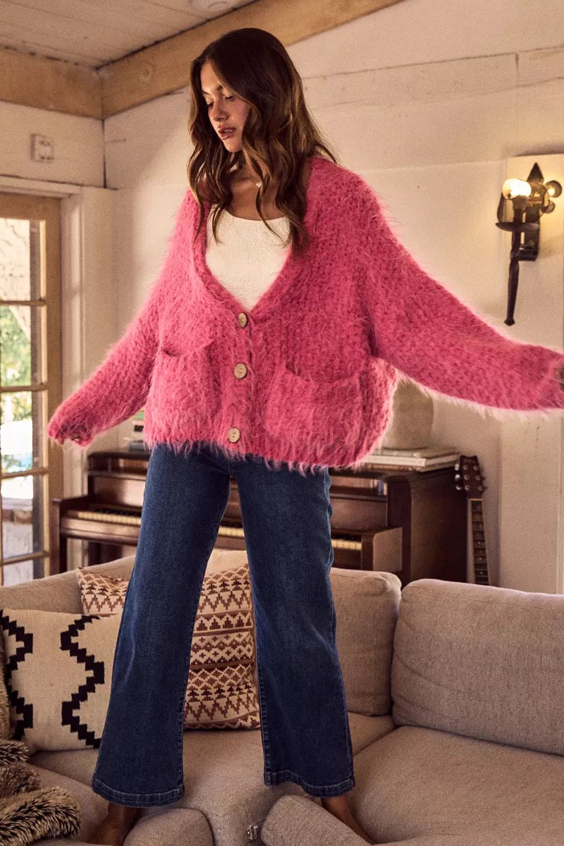 Woman wearing a pink cardigan and blue jeans in a cozy living room.