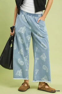 Person wearing light blue denim pants with white patterns on a green background