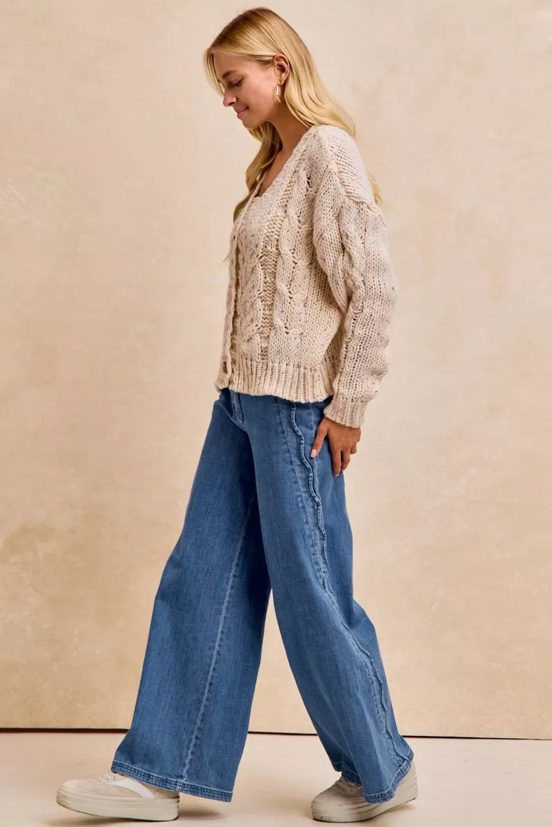 Woman wearing a beige cable knit sweater and blue jeans against a beige background
