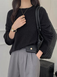 Person wearing a black sweater and gray pants, holding a black handbag.