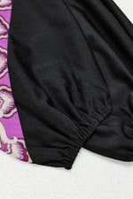 Close-up of black fabric with a pink and purple patterned border.