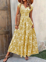Woman wearing a yellow floral dress standing against a textured wall.