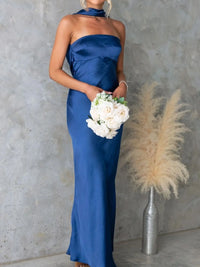 Woman in a blue strapless gown holding flowers against a gray wall with decorative elements.