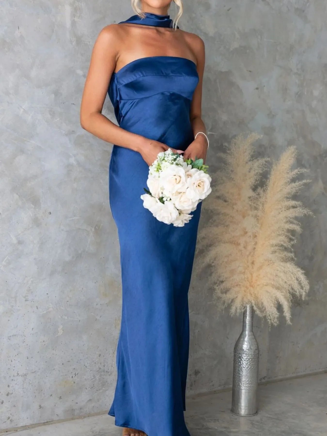 Woman in a blue strapless gown holding flowers against a gray wall with decorative elements.