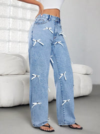 Blue jeans with white bow details worn by a person in a minimalistic room.