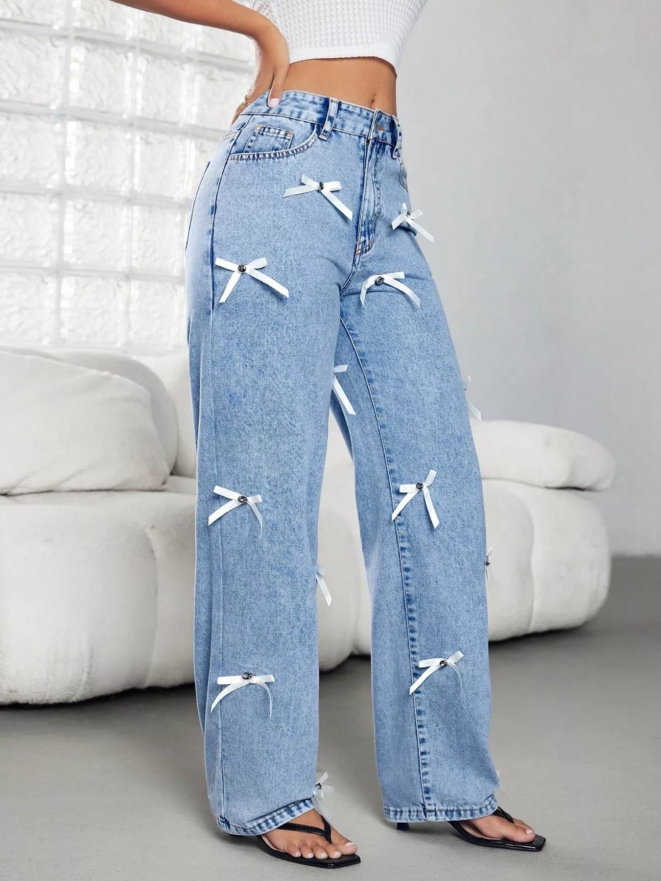Blue jeans with white bow details worn by a person in a minimalistic room.