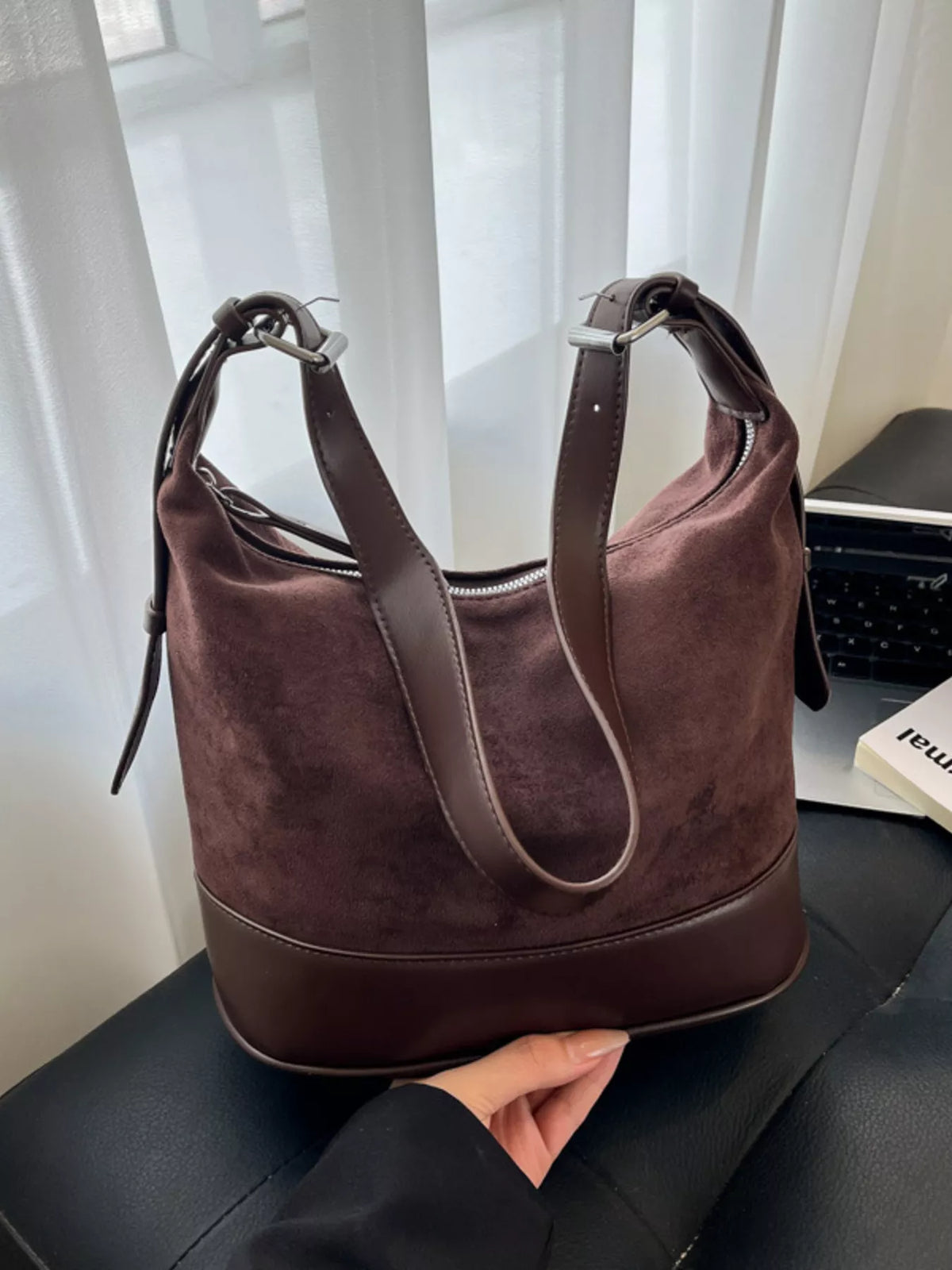 Brown handbag held by a person with a blurred indoor background
