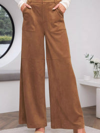 Brown wide-leg pants worn by a person in a minimal indoor setting.