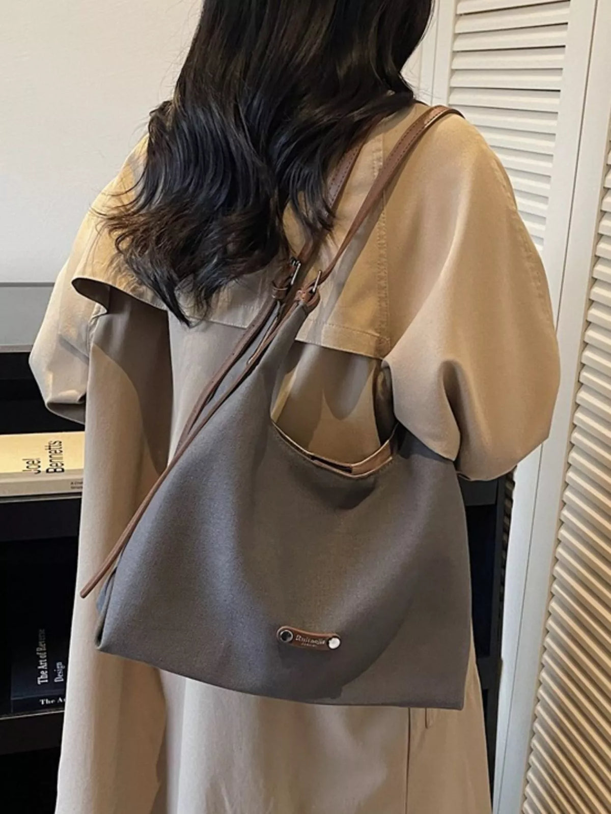 Person wearing a beige coat with a gray shoulder bag indoors.