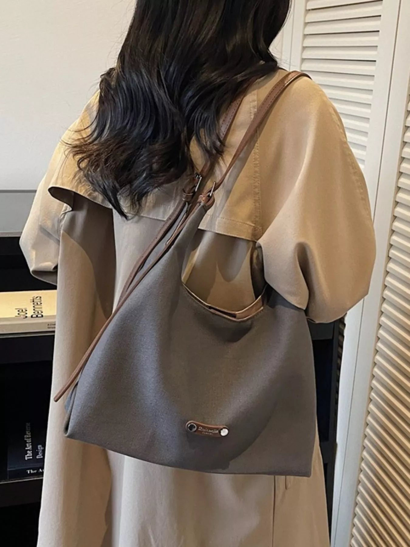 Person wearing a beige coat with a gray shoulder bag indoors.