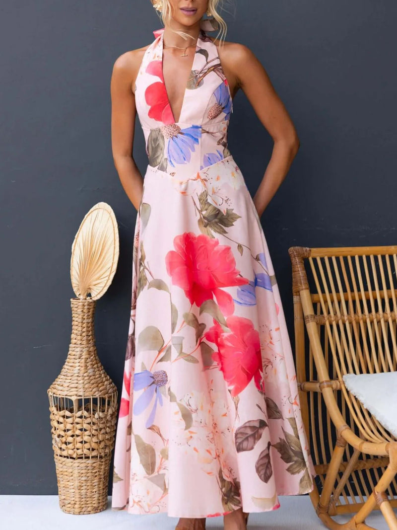 Woman wearing a floral dress standing next to a wicker vase and chair against a dark background