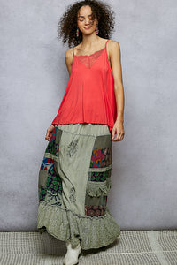 Woman wearing a coral top and patchwork skirt against a gray background