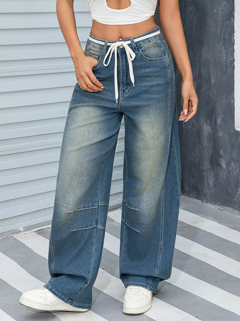 Person wearing wide-leg jeans with a white top and white sneakers on a striped floor.