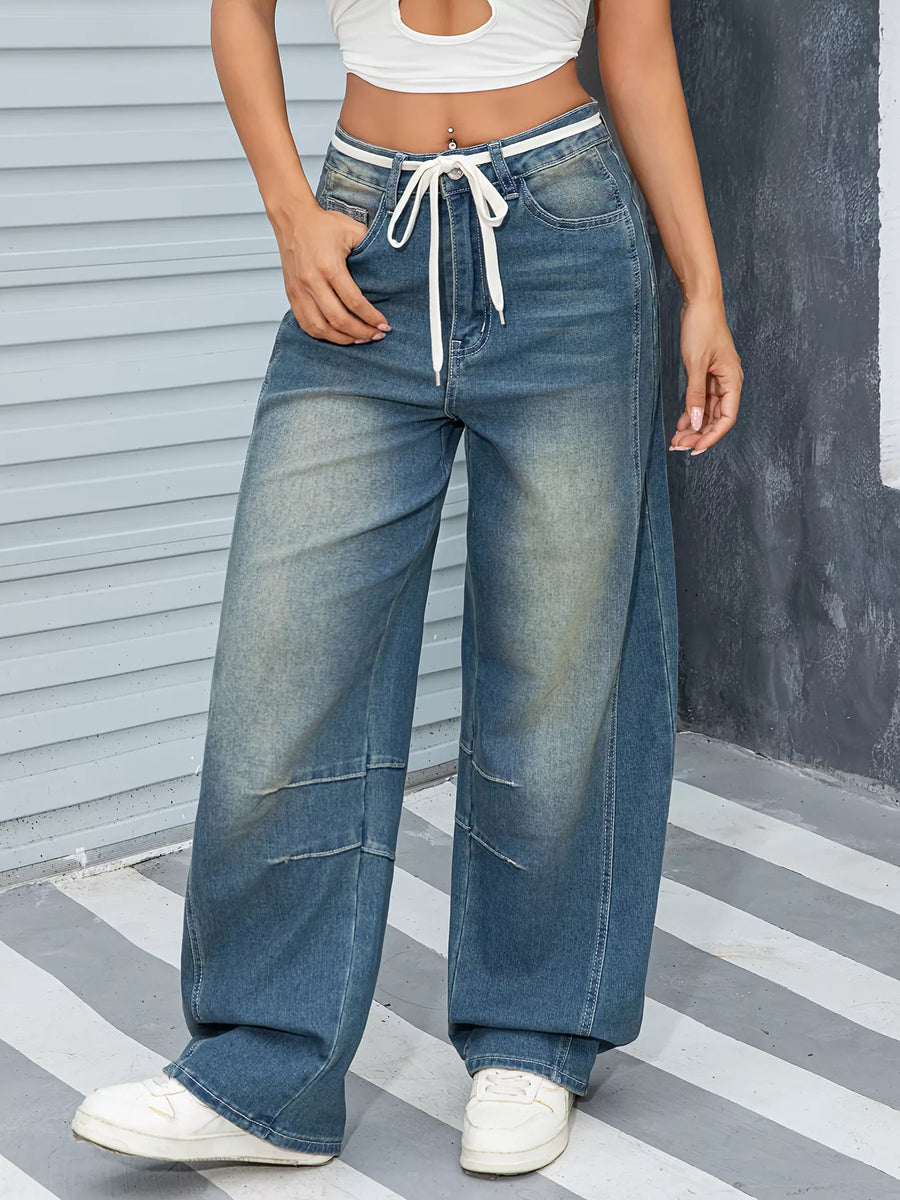 Person wearing wide-leg jeans with a white top and white sneakers on a striped floor.