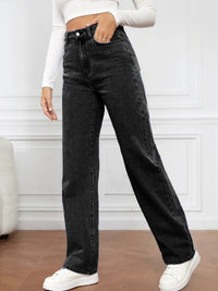 Person wearing black high-waisted jeans and white sneakers in a minimalistic setting