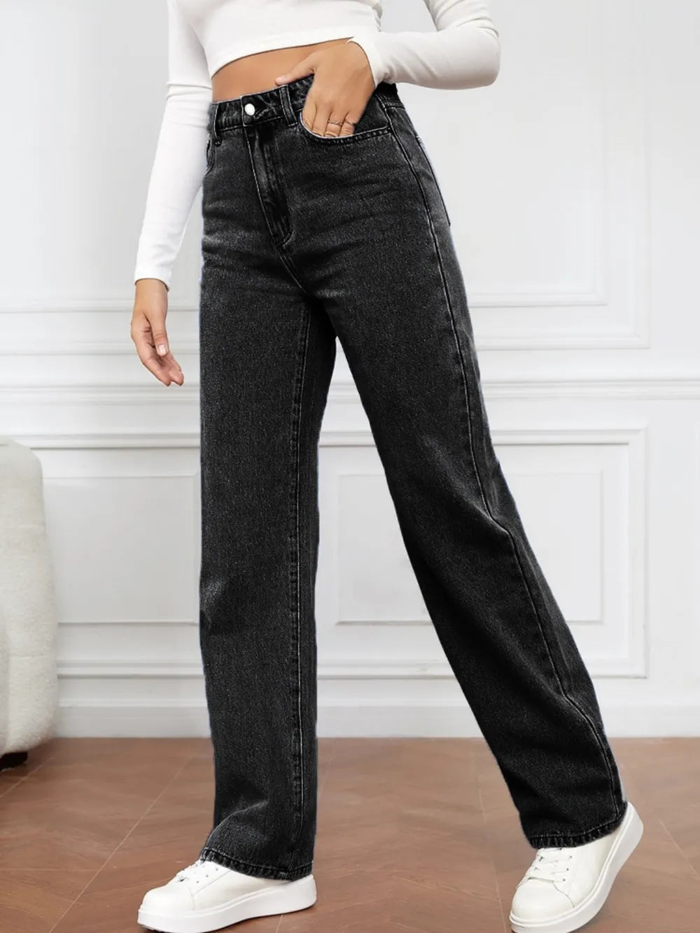 Person wearing black high-waisted jeans and white sneakers in a minimalistic setting