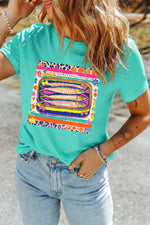 Person wearing a turquoise t-shirt with a colorful graphic design outdoors.