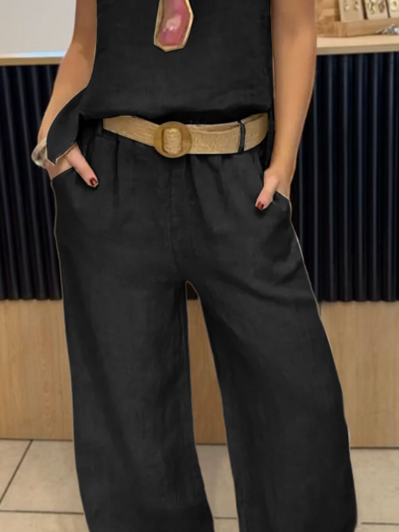 Person wearing a black sleeveless top and wide-leg black pants with a beige belt.