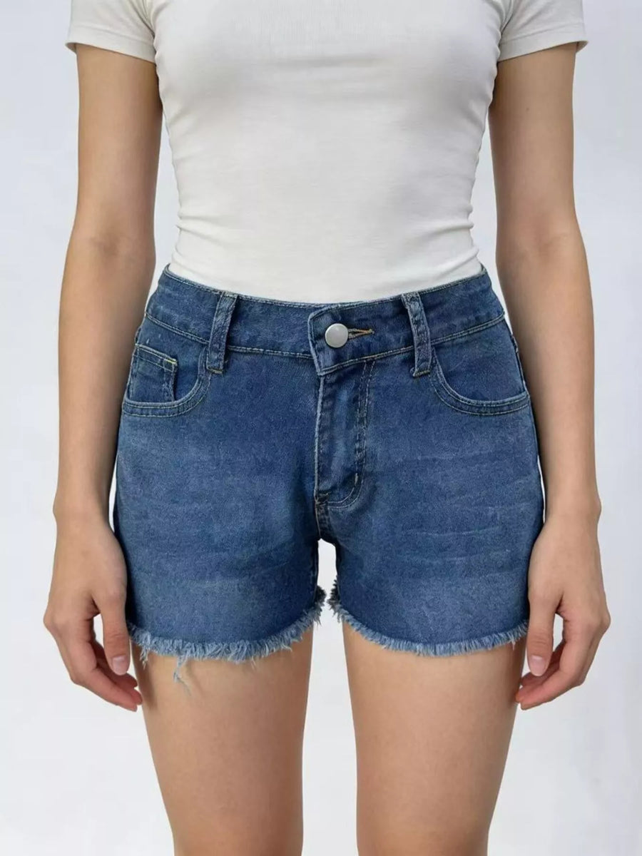 Person wearing blue denim shorts and a white top on a plain background