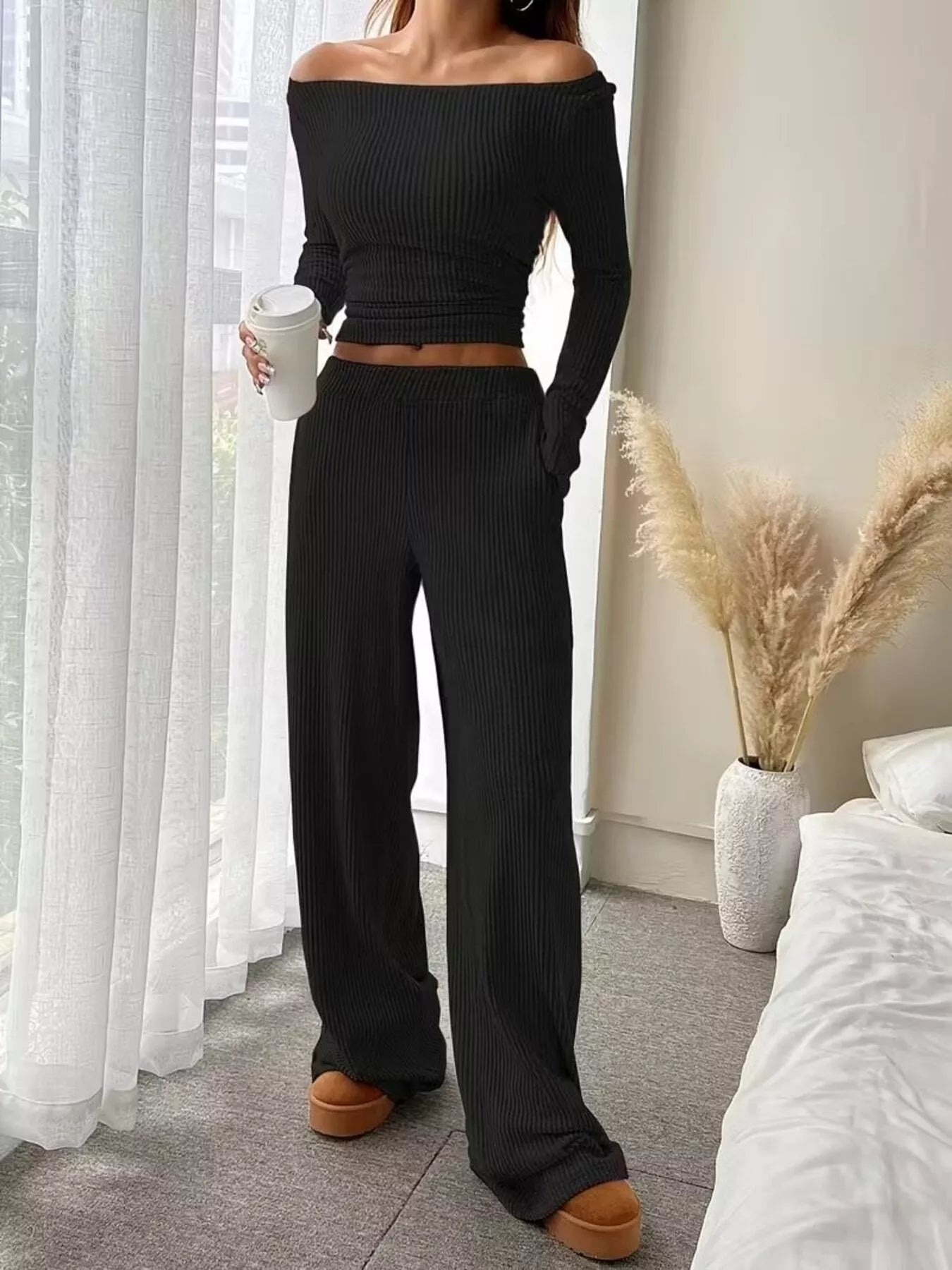 Person wearing a black off-shoulder top and wide-leg pants in a bedroom setting.