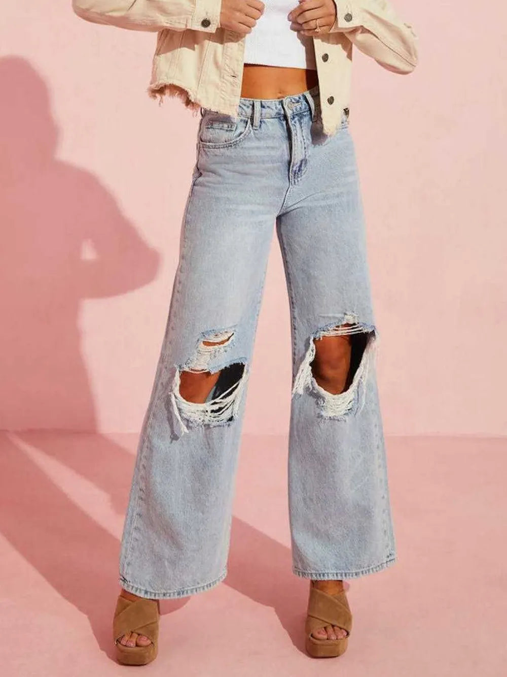 Person wearing light blue ripped jeans on a pink background
