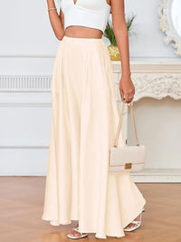 Person wearing a white top and beige skirt holding a white handbag indoors.