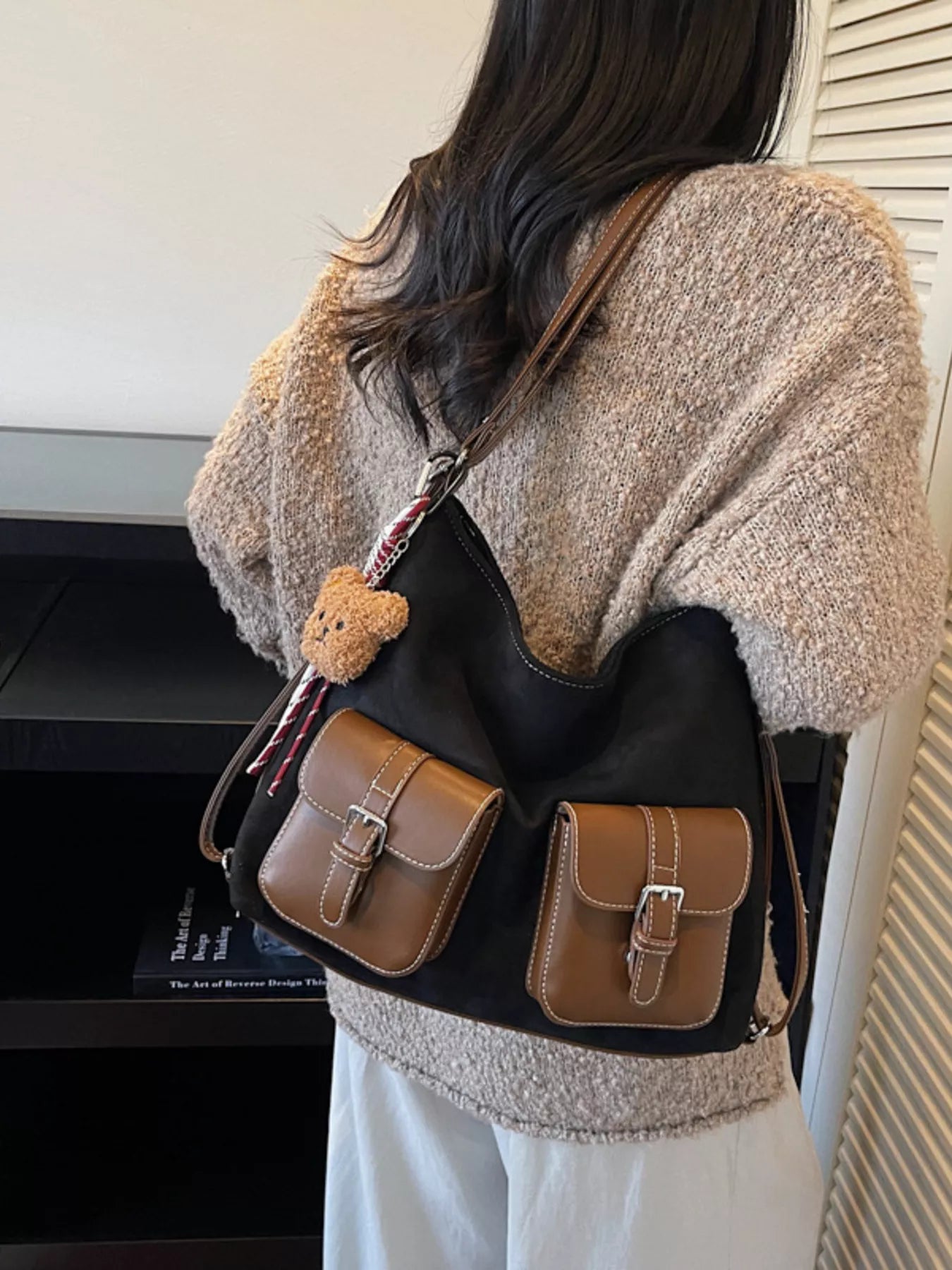 Person wearing a black backpack with brown accents and a teddy bear charm.