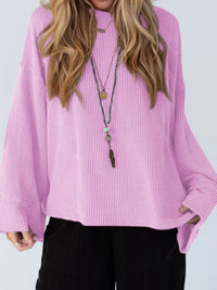 Person wearing a pink ribbed sweater with long sleeves and a necklace on a white background