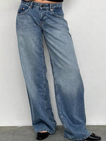 A person wearing light blue wide-leg denim jeans with black shoes, standing against a plain light gray wall.