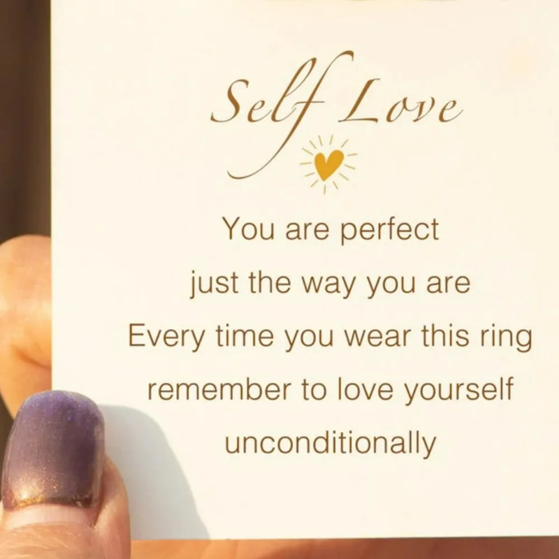 Card with 'Self Love' message and a hand wearing a ring, on a light background.