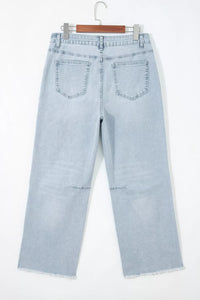 Light blue jeans hanging on a wooden hanger against a white background