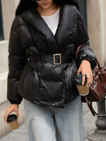 Person wearing a black puffer jacket with a belt, holding coffee cups and a brown bag.