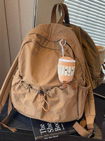Brown backpack with a plush toy on top, placed on a surface with a book underneath.