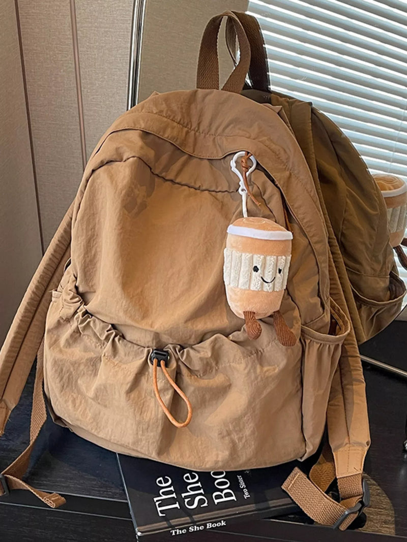 Brown backpack with a plush toy on top, placed on a surface with a book underneath.