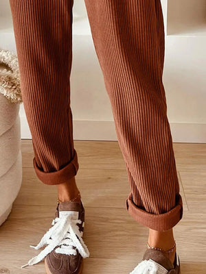 Brown ribbed pants with white sneakers on a wooden floor.