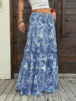 Person wearing a blue paisley skirt standing on a wooden deck.