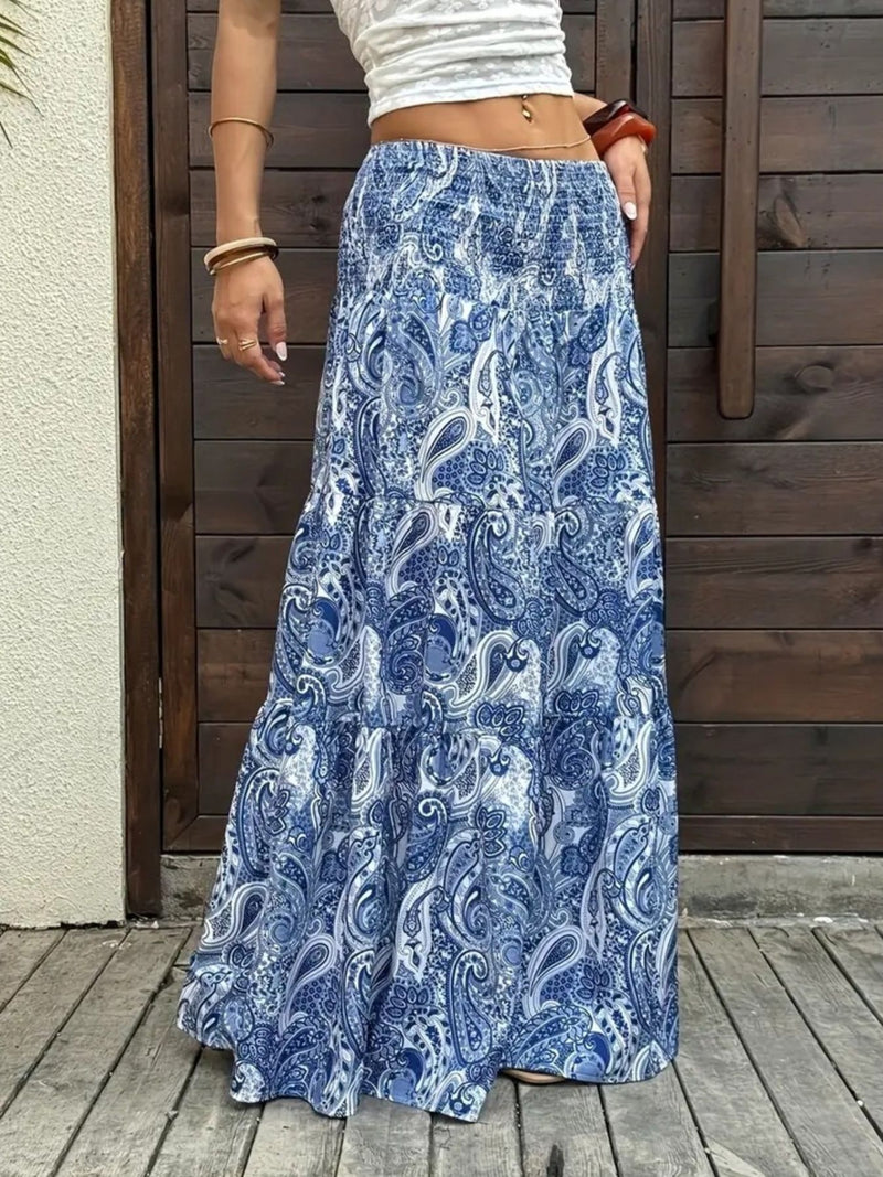 Person wearing a blue paisley skirt standing on a wooden deck.