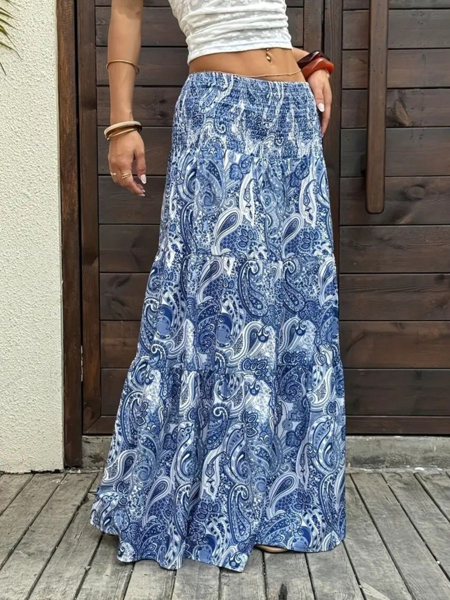 Person wearing a blue paisley skirt standing on a wooden deck.