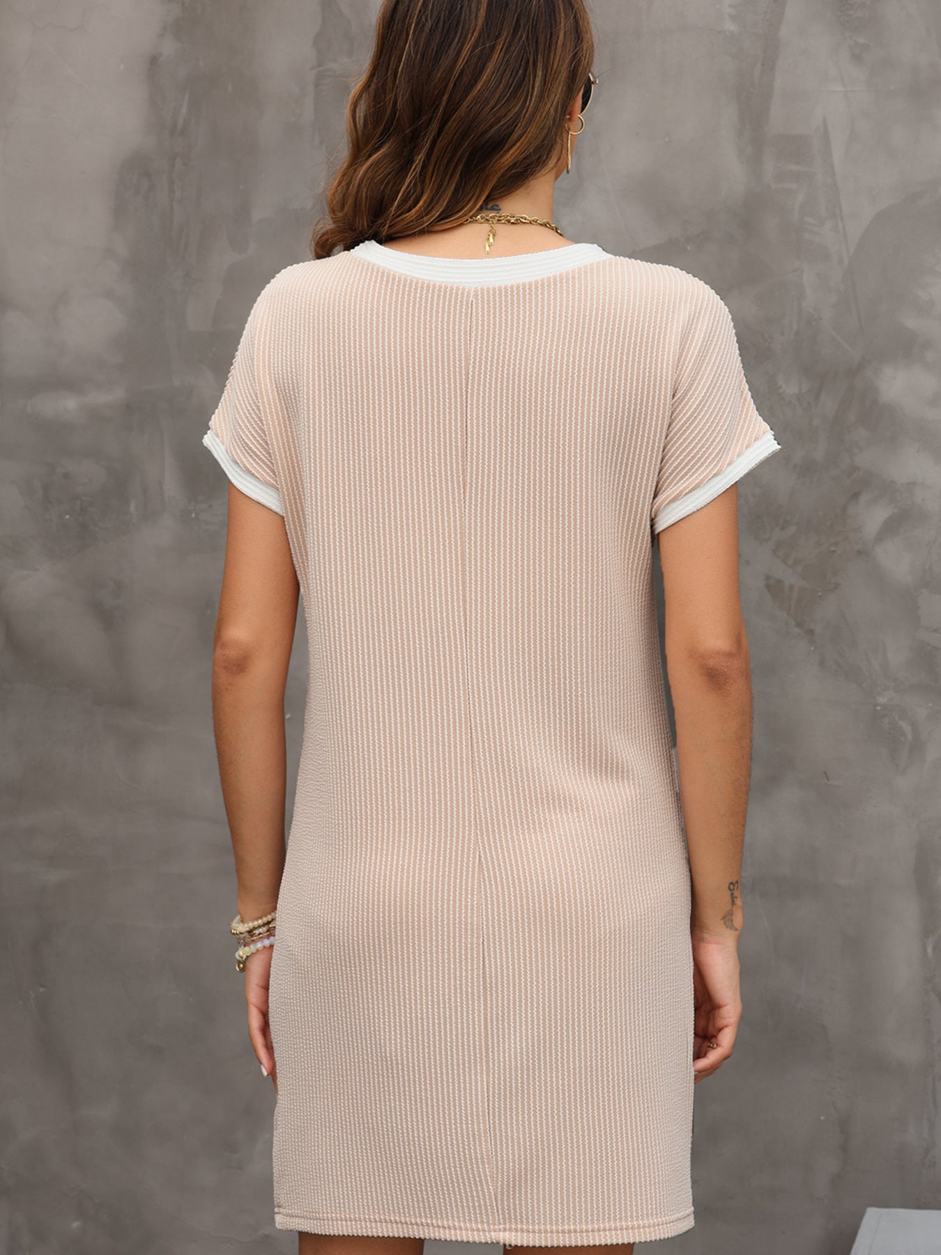 Woman wearing a beige ribbed dress against a gray concrete wall