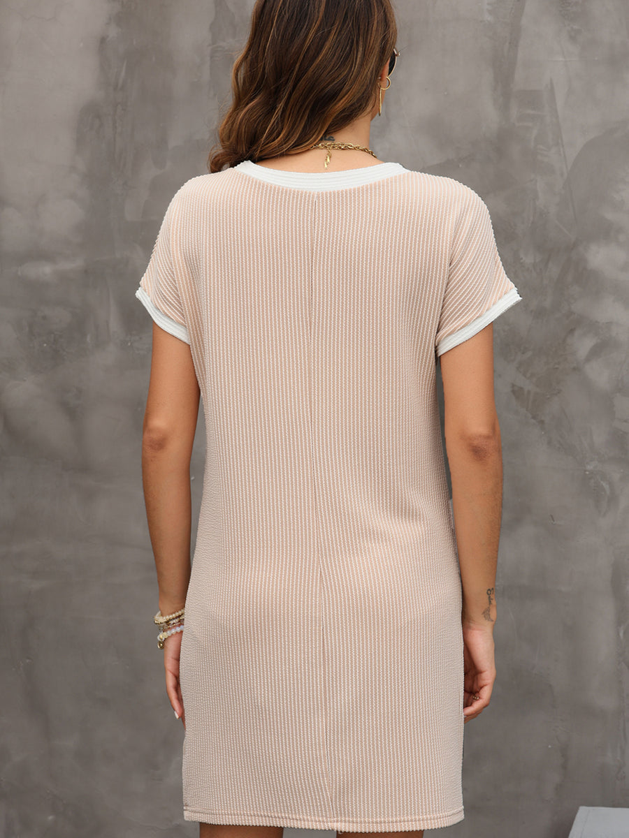 Woman wearing a beige ribbed dress against a gray concrete wall