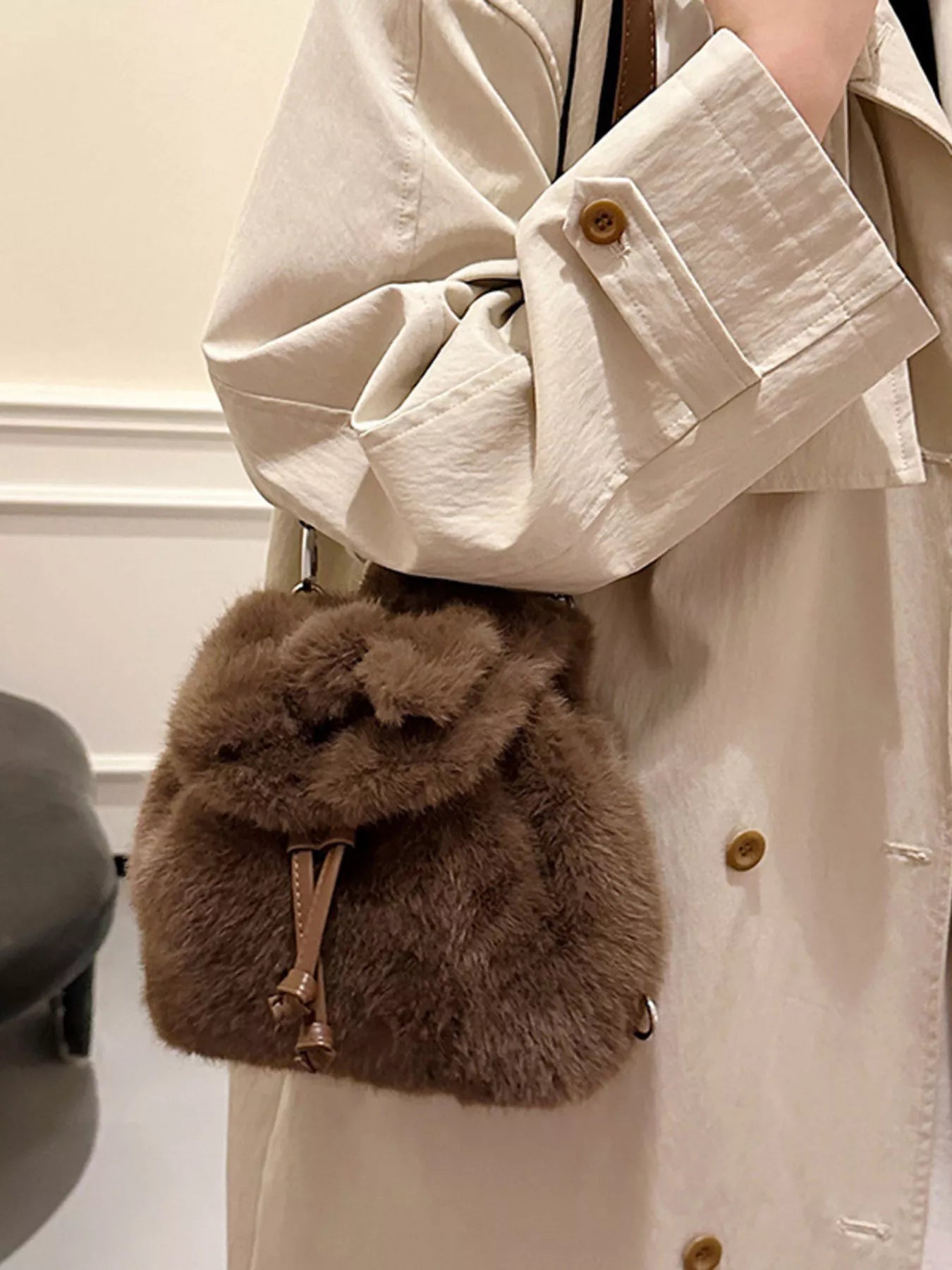 Brown fluffy pouch held by a person wearing a beige coat.