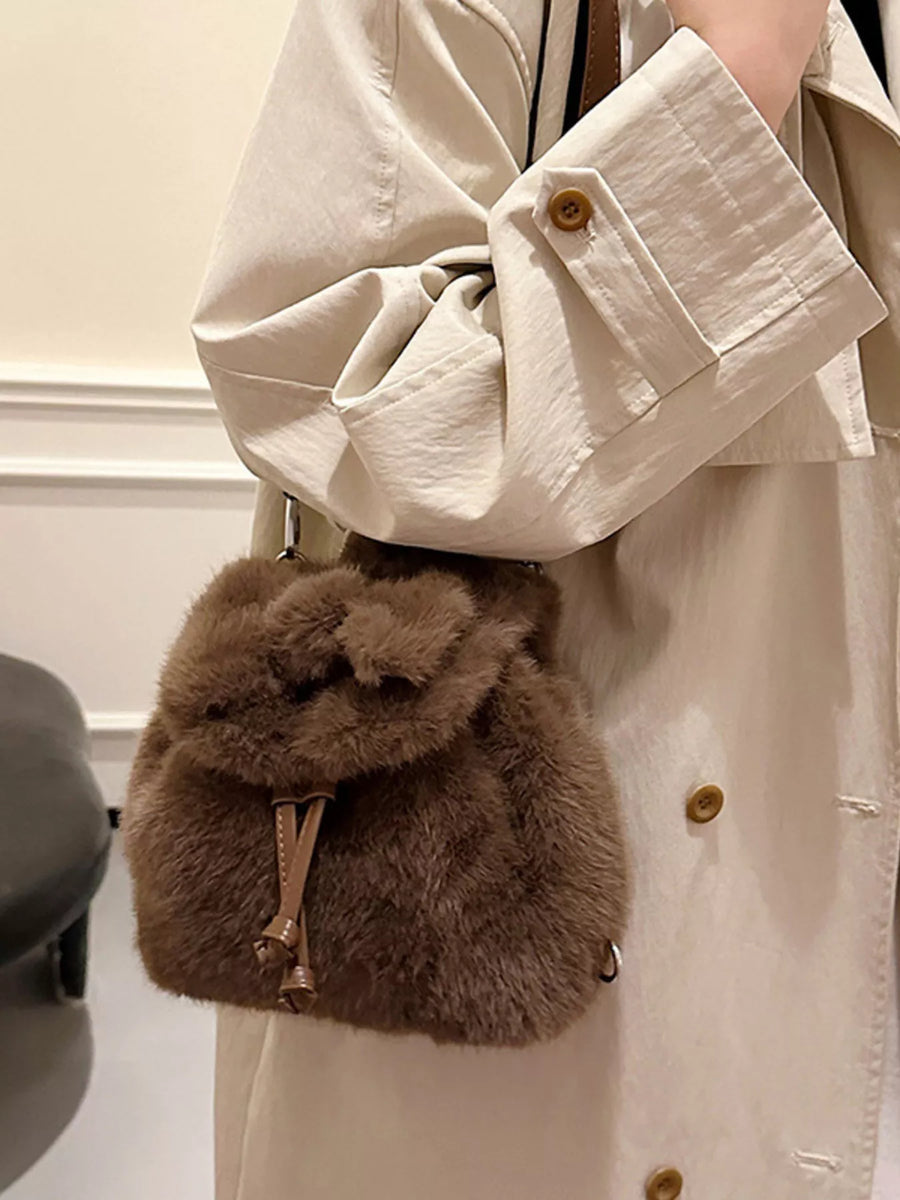 Brown fluffy pouch held by a person wearing a beige coat.