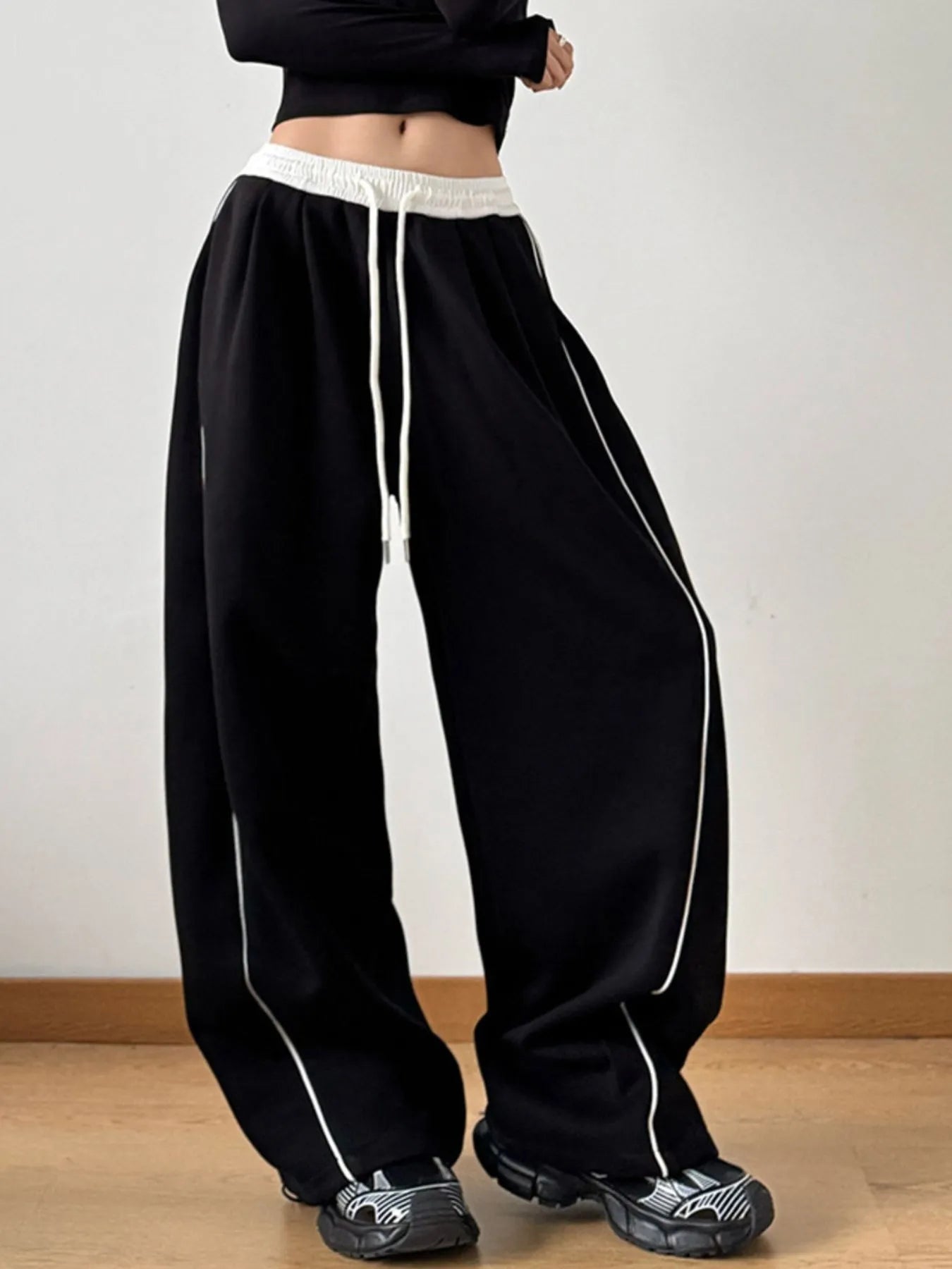 Black wide-leg pants with white trim worn by a person on a plain background