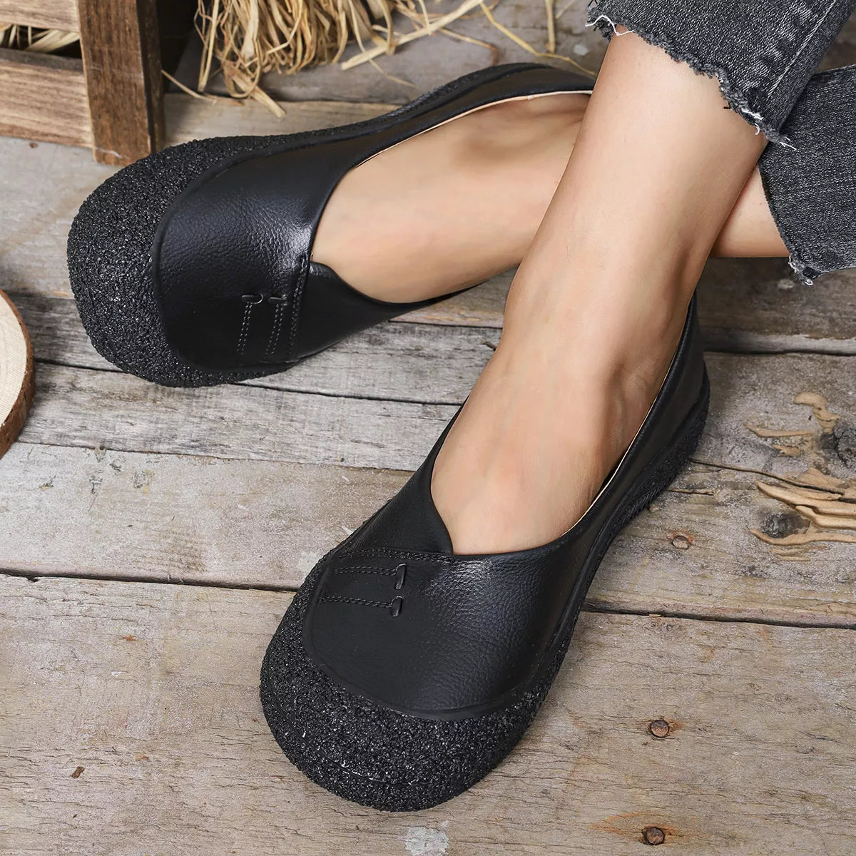 Black flat shoes worn by a person on a wooden floor