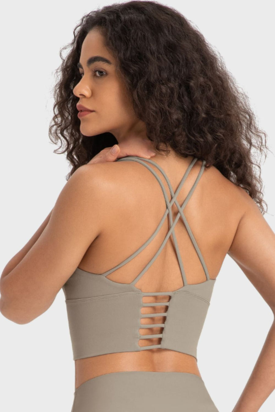 Woman wearing a beige sports bra with criss-cross straps on a light gray background