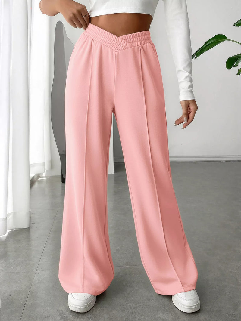 Person wearing pink wide-leg pants and white sneakers in a minimal indoor setting.