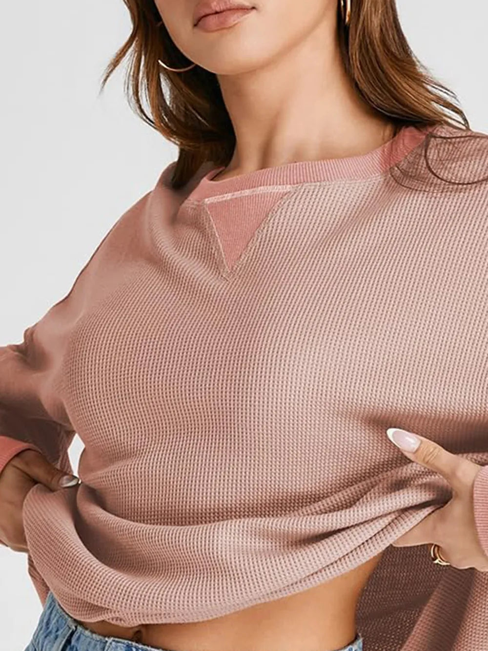 Person wearing a pink textured sweater with a plain background