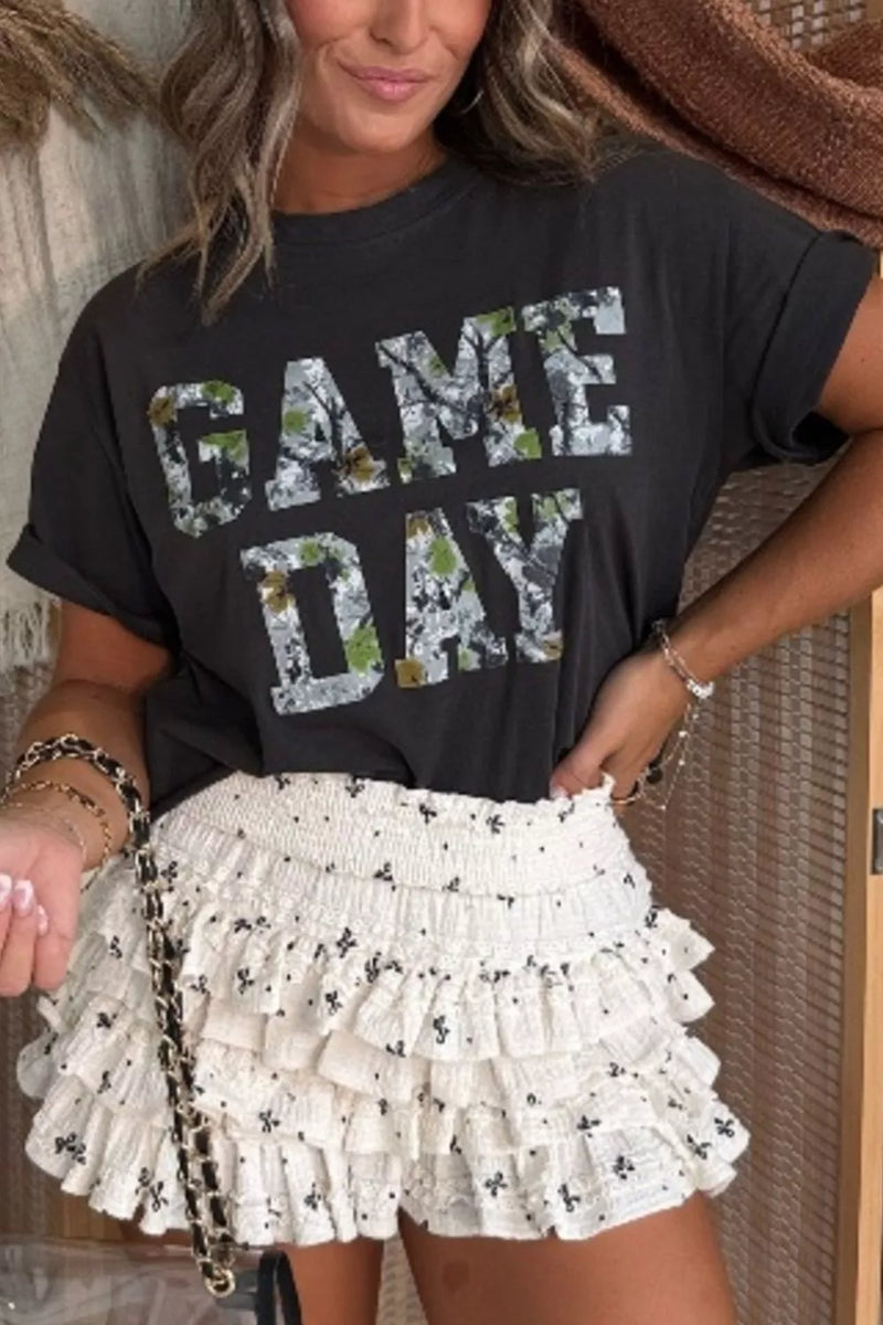 Person wearing a black 'GAME DAY' t-shirt with floral text and a white ruffled skirt.