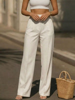Person wearing a white top and wide-leg pants holding a woven bag on a street.