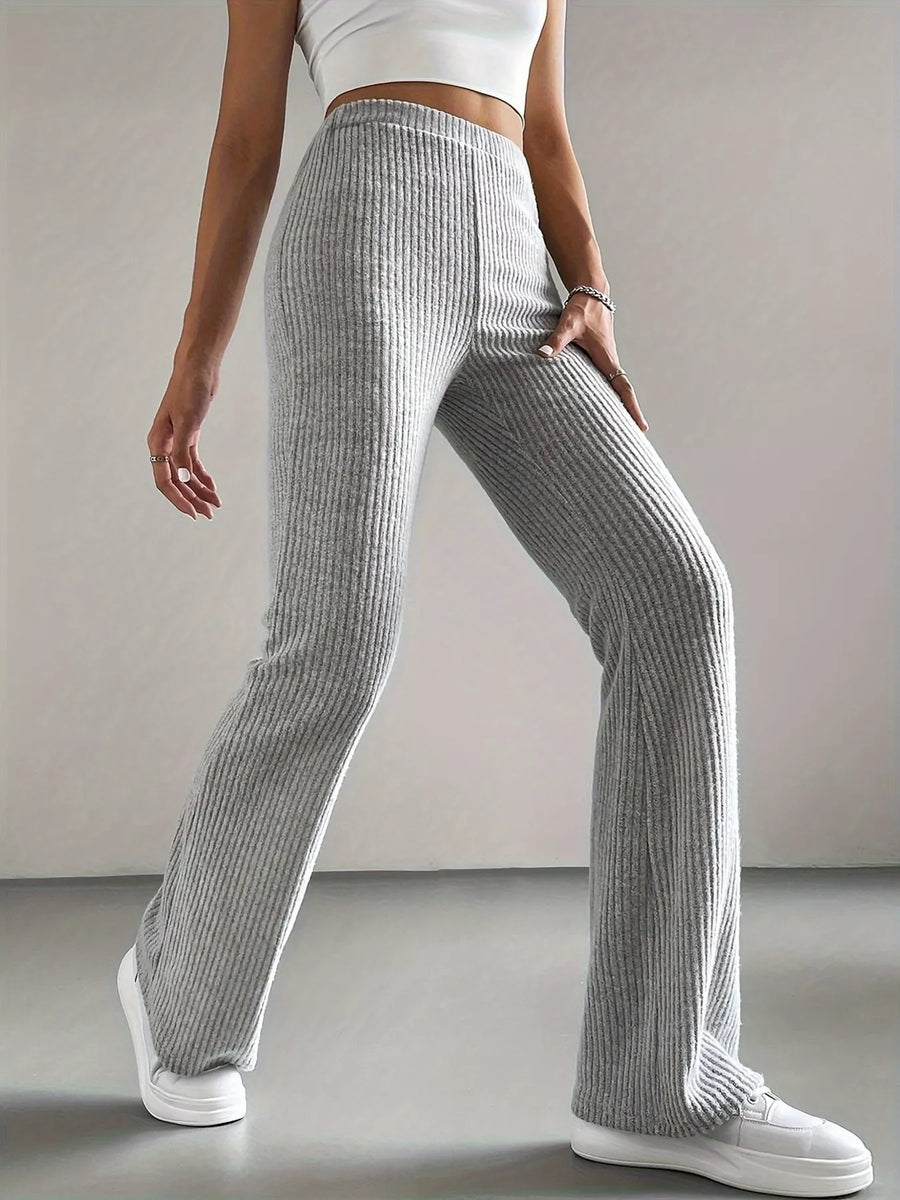 Person wearing gray ribbed pants and white sneakers on a plain background